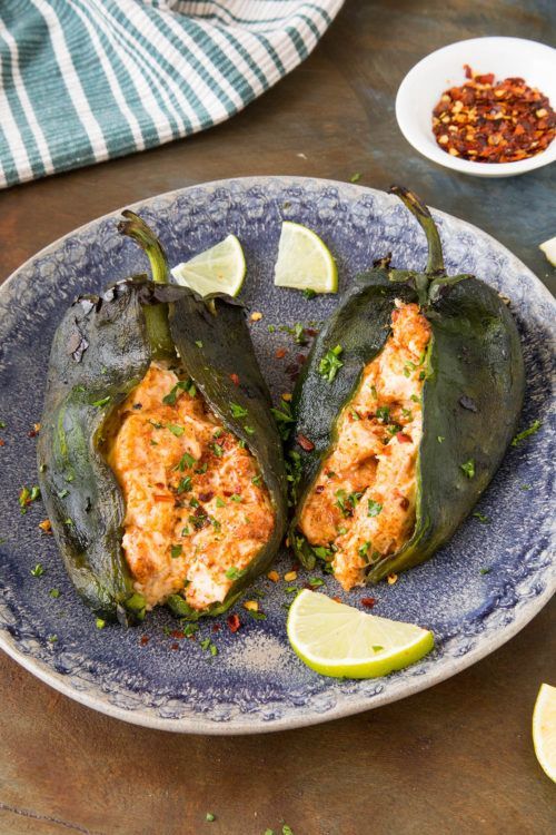 Two cream cheese stuffed poblano peppers on a blue plate.