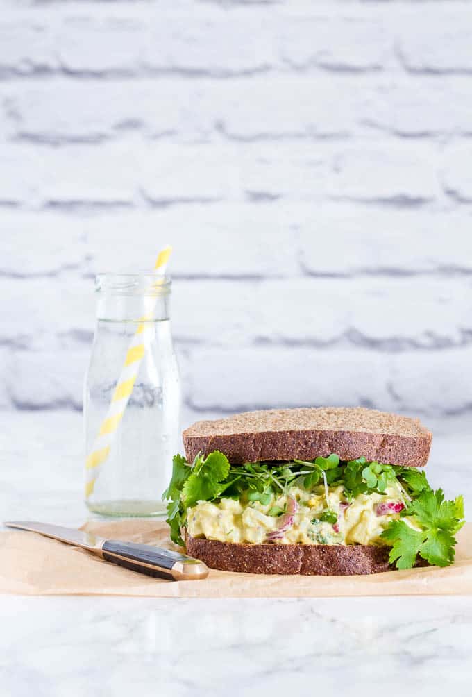 An egg salad sandwich next to a jug of water.