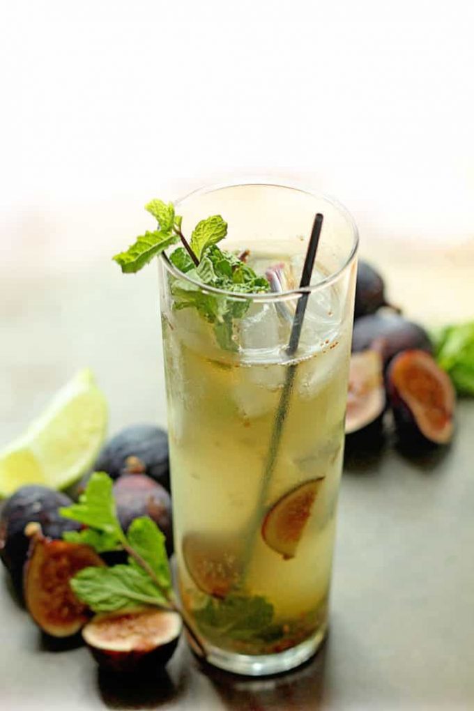 A fig mojito in a tall glass. Fresh figs are scattered around the glass.