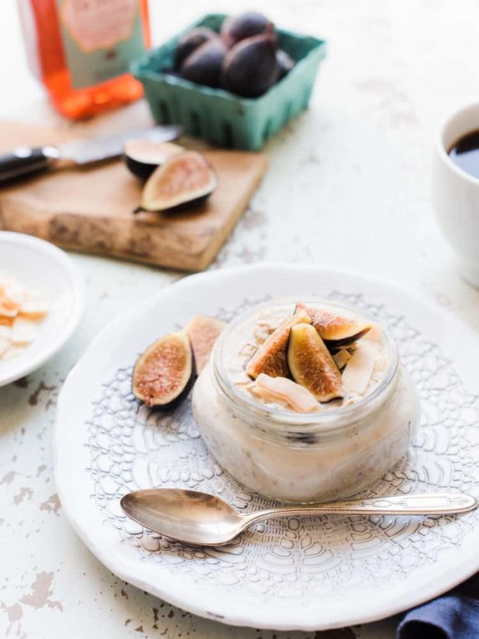 A small jar of fig overnight oats topped with fresh figs, resting on a white plate next to a spoon.