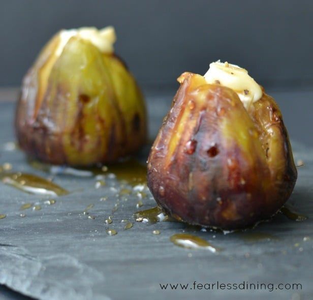 Two grilled figs stuffed with Brie cheese and drizzled with honey on a gray surface.