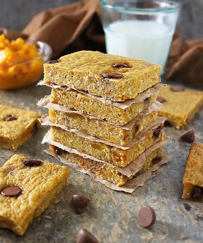 A stack of five kabocha chocolate chip bars. A glass of milk rests in the background. More bars are scattered around the stack.