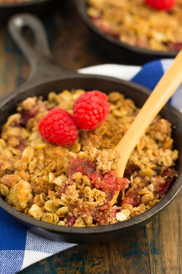 A mini raspberry rhubarb crisp in a small cast iron skillet. A wood spoon rests in the skillet.