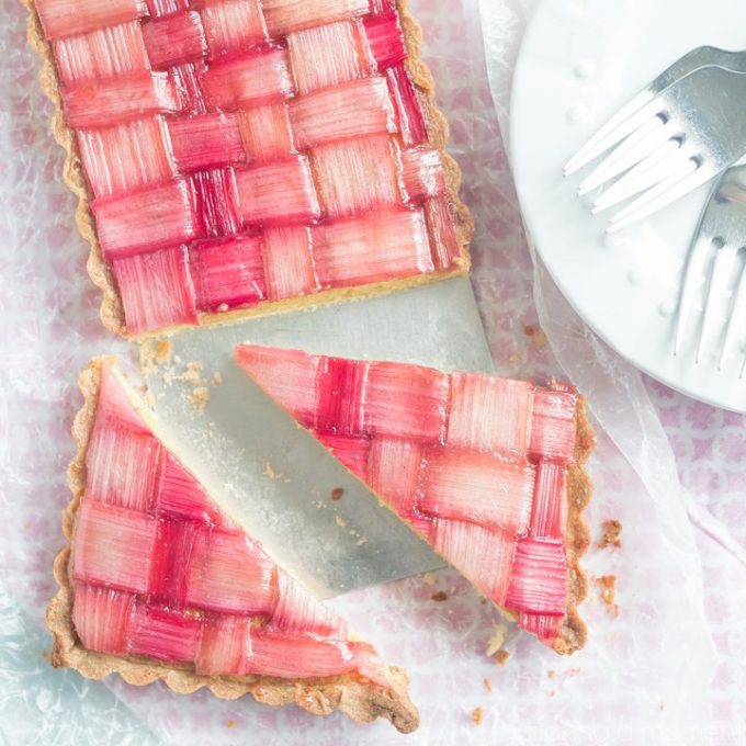 Sliced rhubarb tart next to a white plate with forks on it.