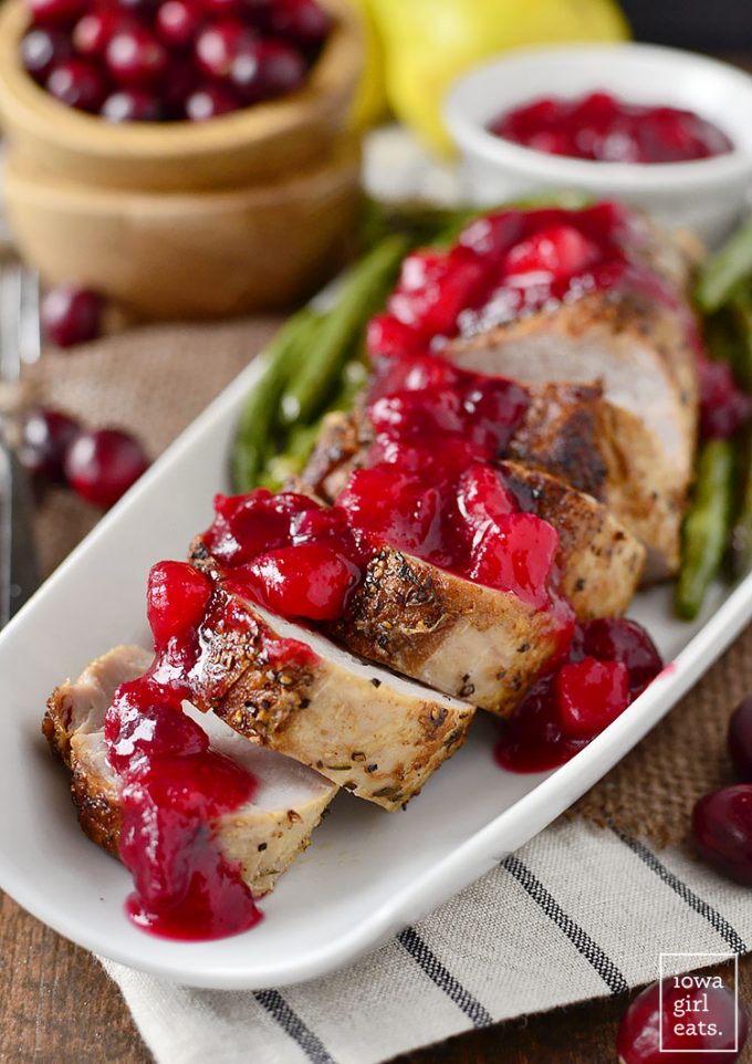 Roasted pork tenderloin with cranberry sauce on a white platter.