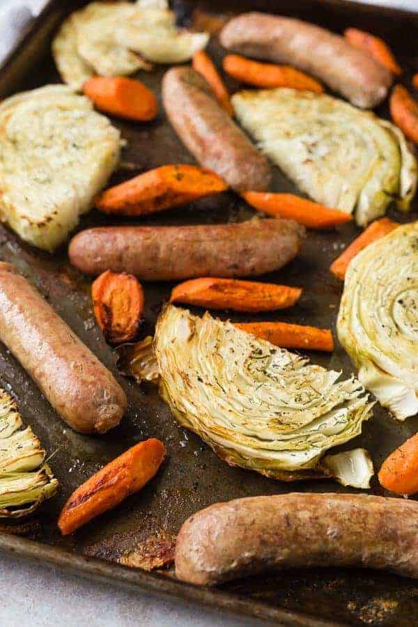 Cabbage wedges, carrots, and sausages on a sheet pan.