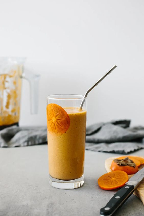 A persimmon smoothie in a glass with a straw.