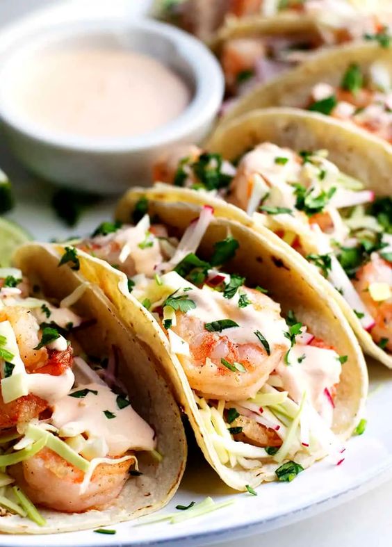 A plate of spicy shrimp tacos with a dish of sauce.