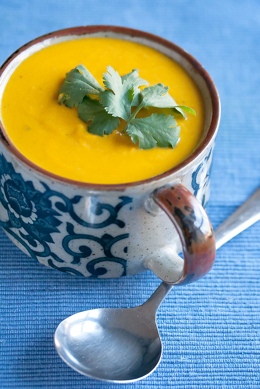 A mug full of Thai kabocha soup, with a spoon resting nearby.