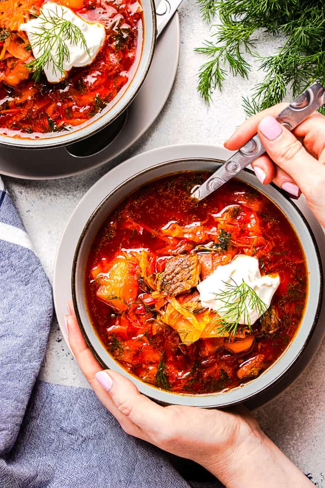 Overhead view of hands being wrapped around a bowl of borscht soup.