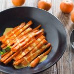 Tequila carrots with tahini sauce on a dark gray plate.
