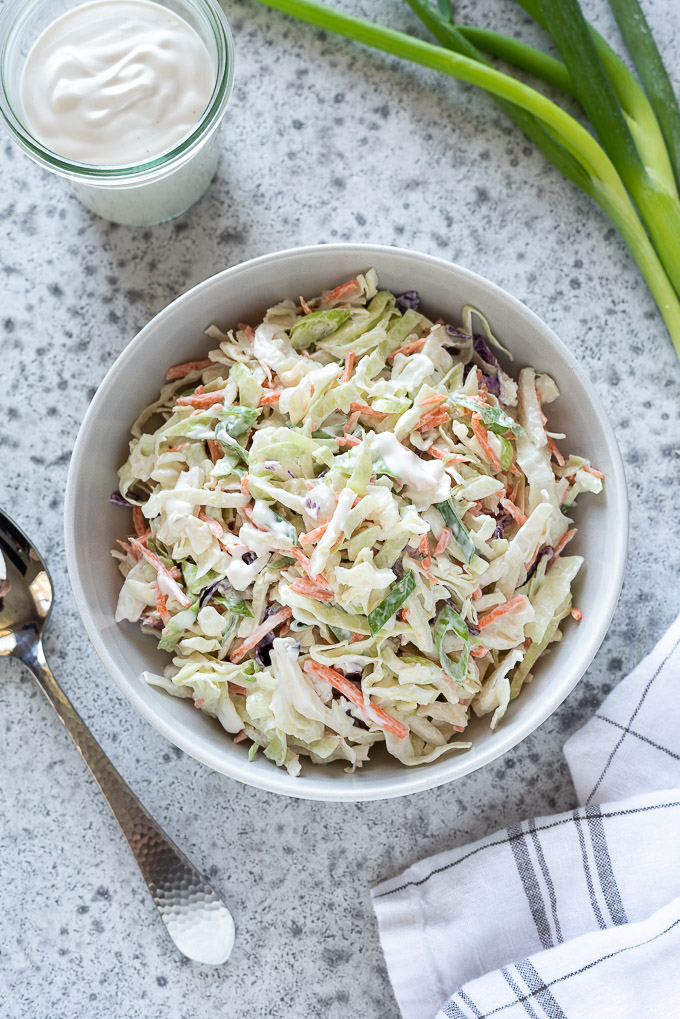 Coleslaw in a white bowl with dressing and green onions