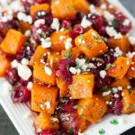 Roasted butternut squash with cranberries and feta on a white platter.