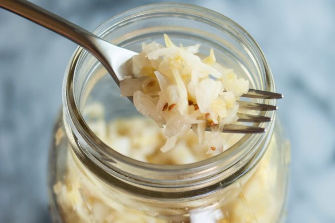 A forkful of sauerkraut above a mason jar.