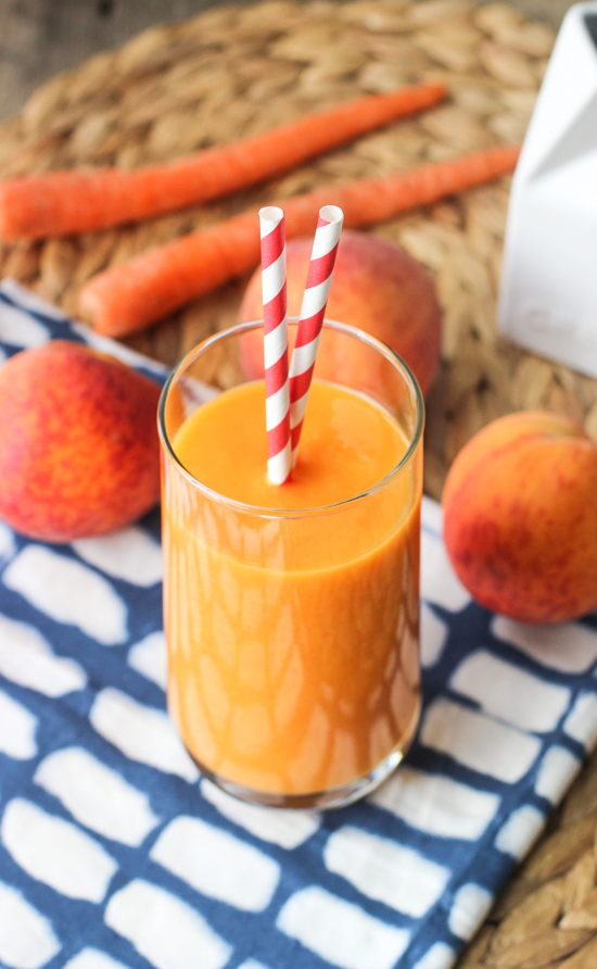 A peach mango carrot smoothie in a glass with two paper striped straws.