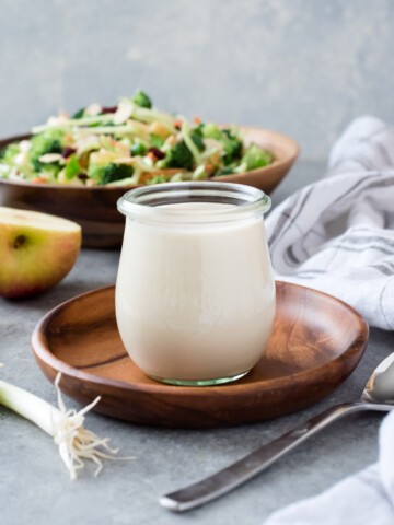 Coleslaw dressing in a jar with broccoli salad behind