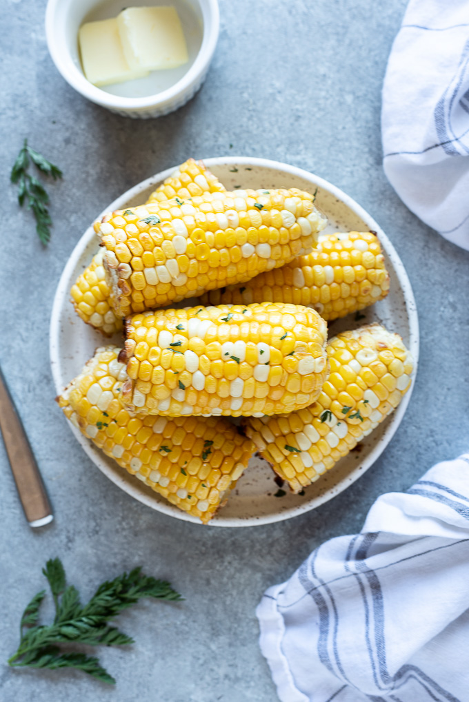 Air fryer corn on the cob on a white plate with butter and parsley