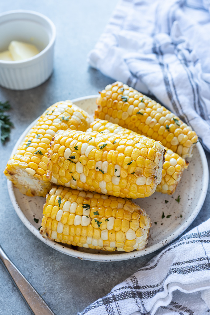 Air fryer corn on the cob on a serving plate with a linen alongside