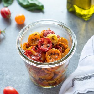 Oven roasted cherry tomatoes in a jar with basil and olive oil behind