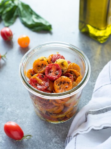 Oven roasted cherry tomatoes in a jar with basil and olive oil behind