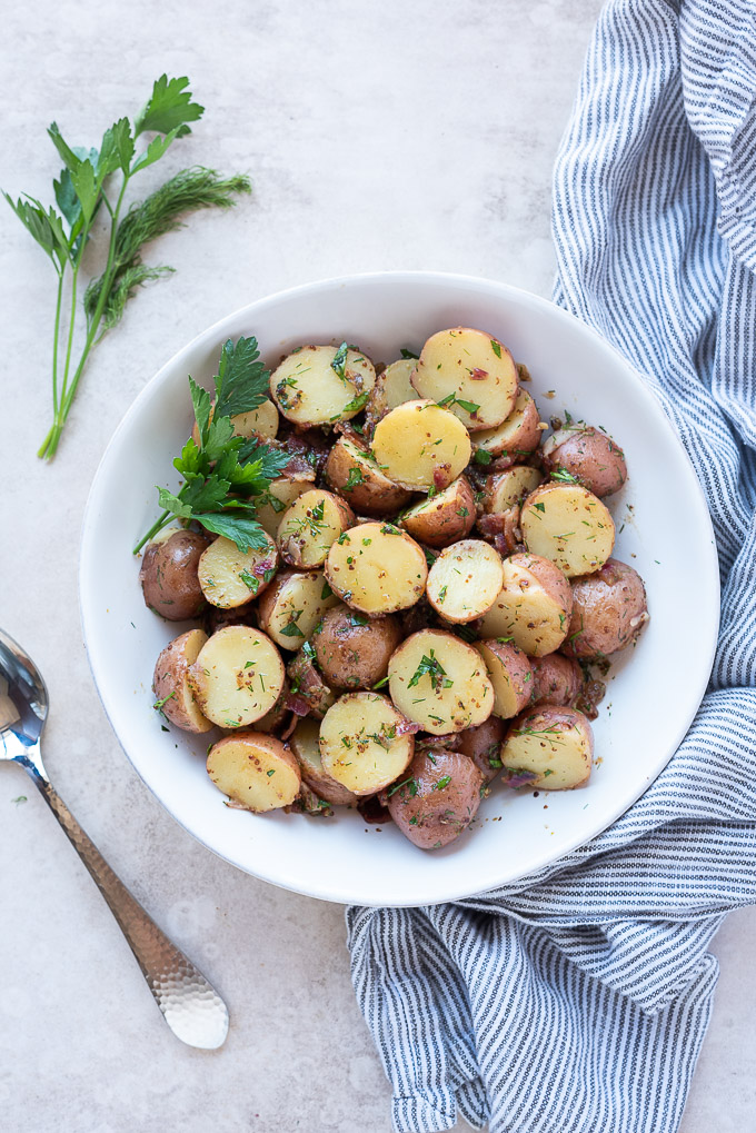 German potato salad in a white bowl with herbs and a linen
