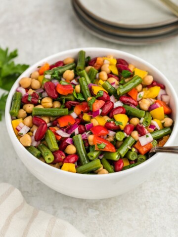 Three bean salad in white bowl with spoon inside