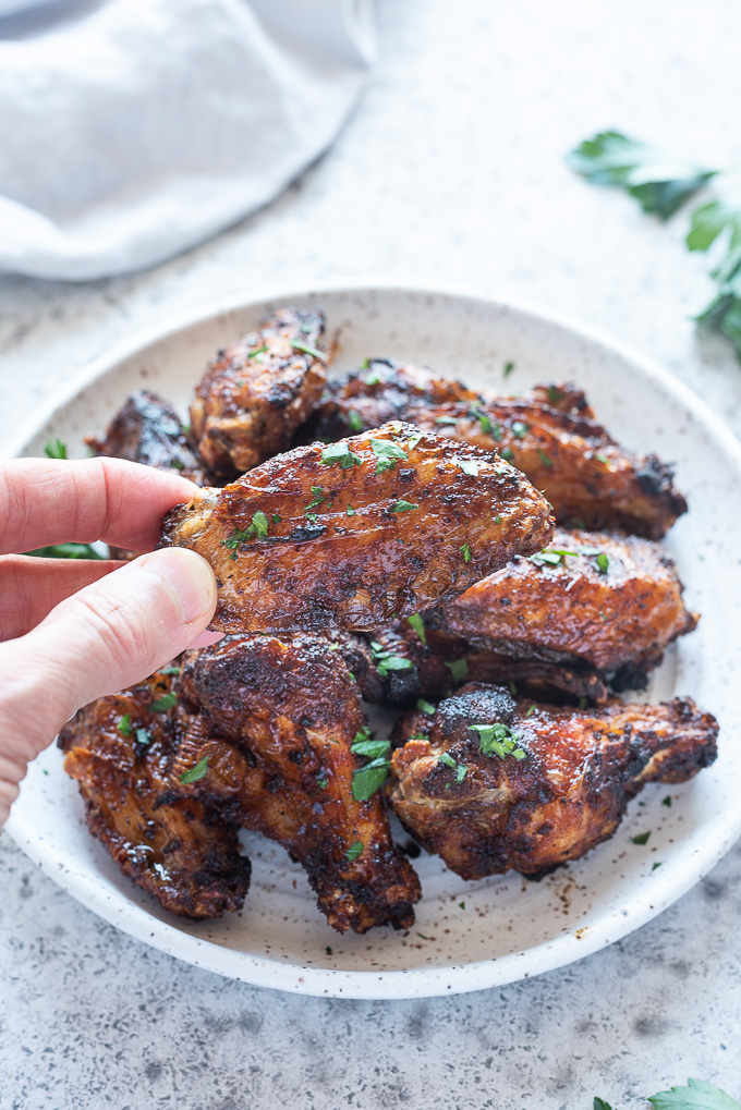 Hand holding air fryer chicken wing above plate of wings