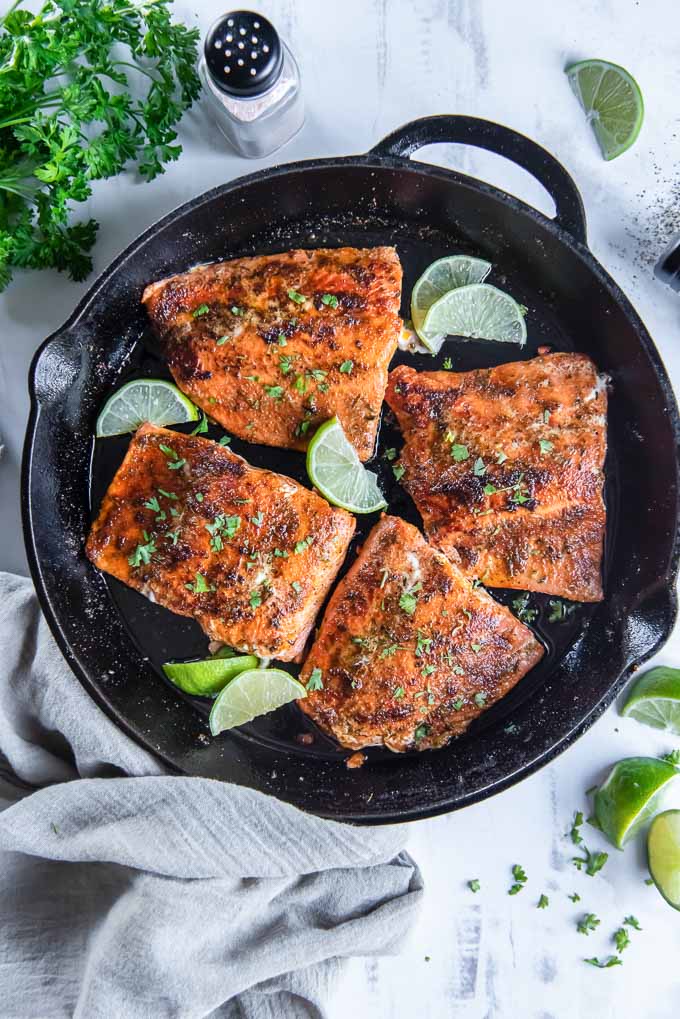 Blackened salmon filets in a cast iron skillet with limes