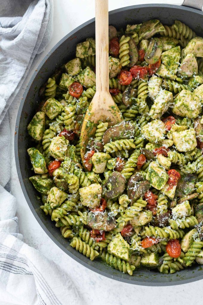 Chicken pesto pasta in a skillet with wooden spoon