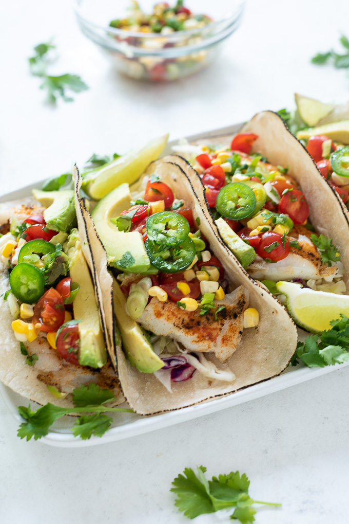 Grilled fish tacos on a plate with salsa, lime and cilantro