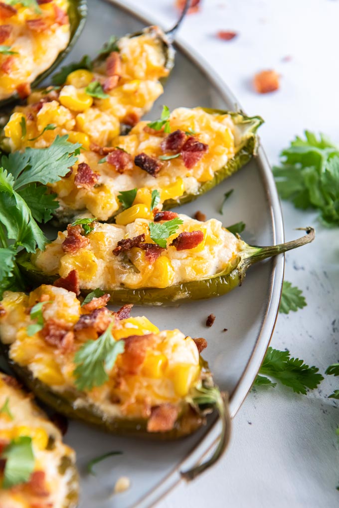Corn dip stuffed jalapeño peppers on a gray plate with bacon and cilantro