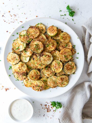 Oven baked zucchini chips on a plate with a linen alongside