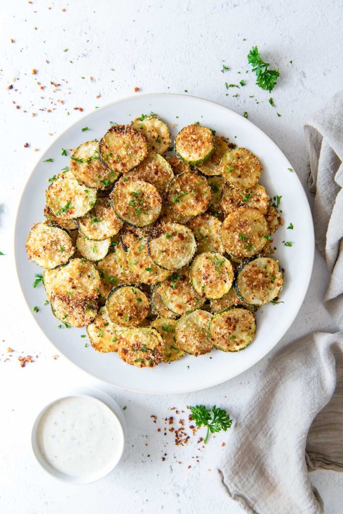 Oven baked zucchini chips on a plate with a linen alongside