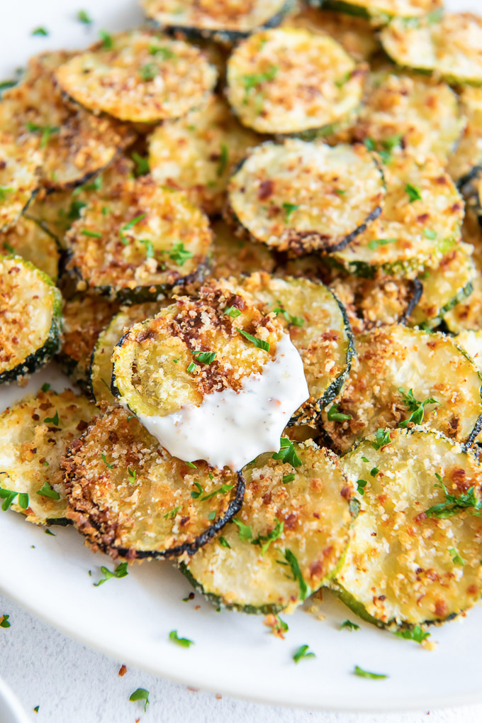 Plate of zucchini chips with one coated with ranch dressing