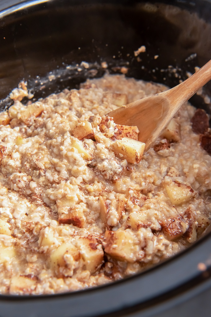 Wooden spoon digging into crockpot steel cut oats with apple