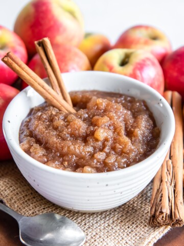 Homemade applesauce in a white bowl with cinnamon sticks