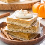 Stack of pumpkin pie bars on a plate topped with whipped cream