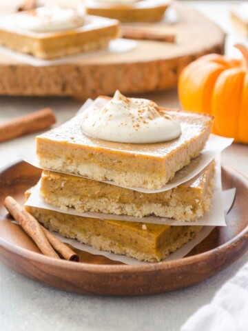 Stack of pumpkin pie bars on a plate topped with whipped cream