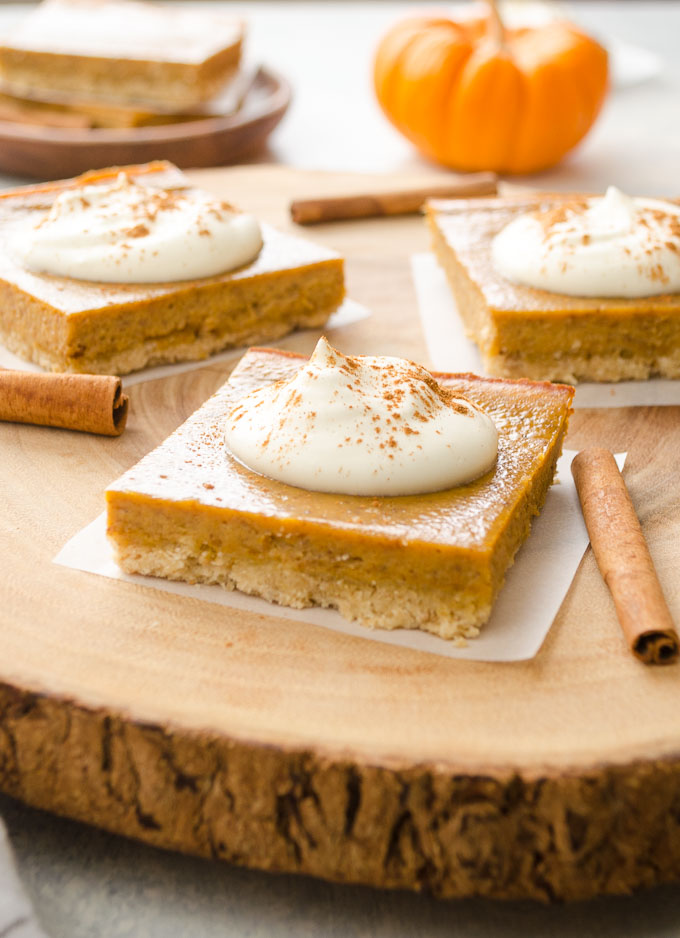 Pumpkin pie bars on a wooden server with whipped cream and cinnamon sticks