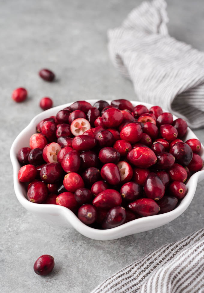 Fresh cranberries in a white bowl with some cut in half