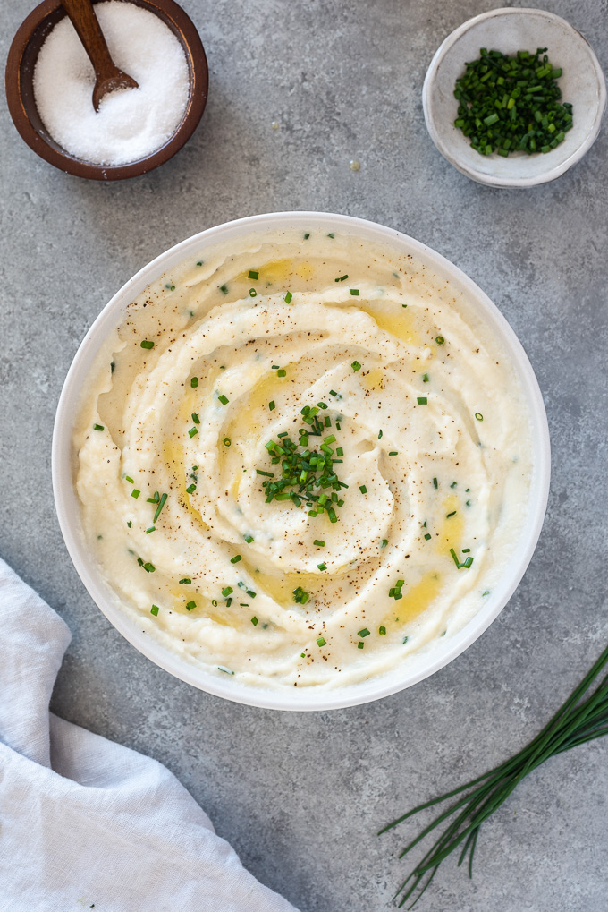 Garlic mashed cauliflower in a white serving bowl with chives