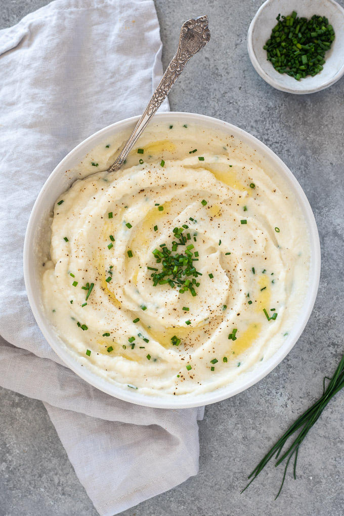 Garlic mashed cauliflower in a bowl topped with butter and chives