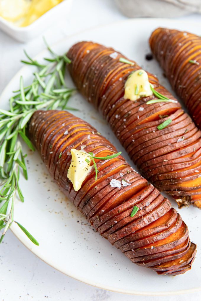 Hasselback sweet potatoes on a plate with butter and rosemary