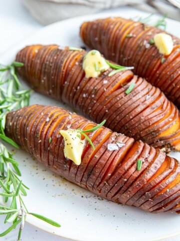 Three hasselback sweet potatoes on a white plate