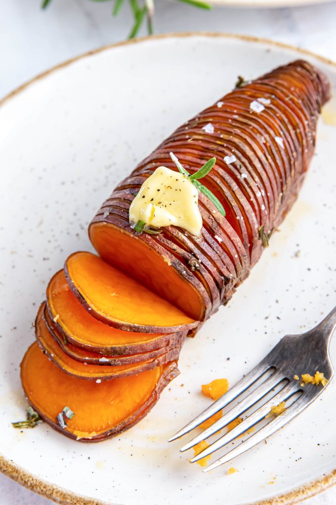 Rosemary hasselback sweet potato on a plate with butter on top