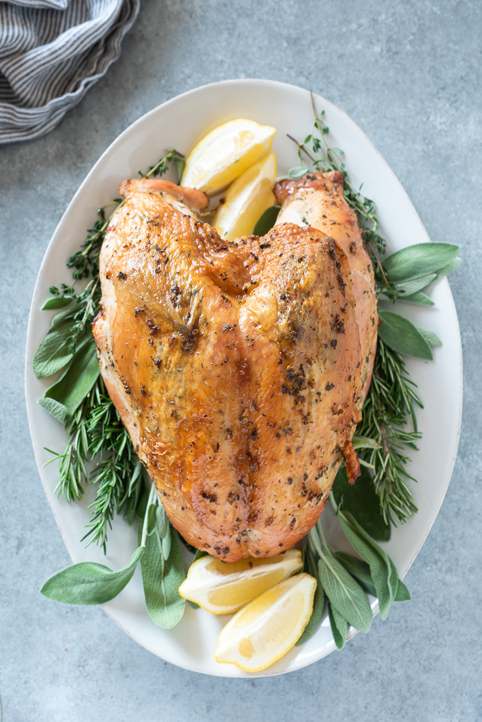 Roast turkey breast on a serving platter with herbs and lemon
