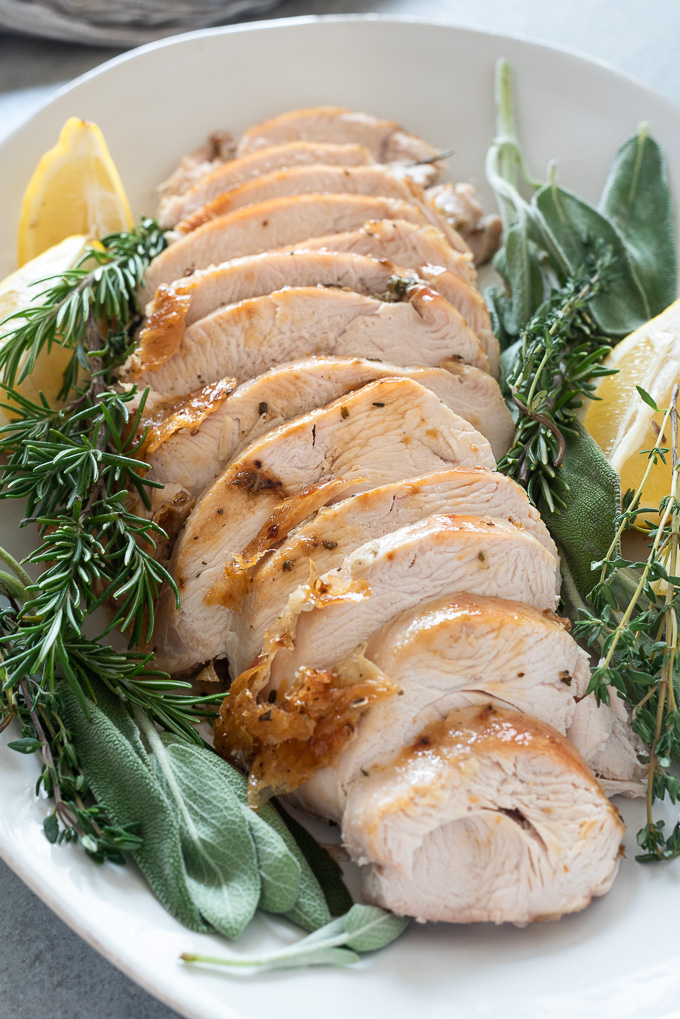 Oven roasted turkey breast sliced on a serving platter with herbs