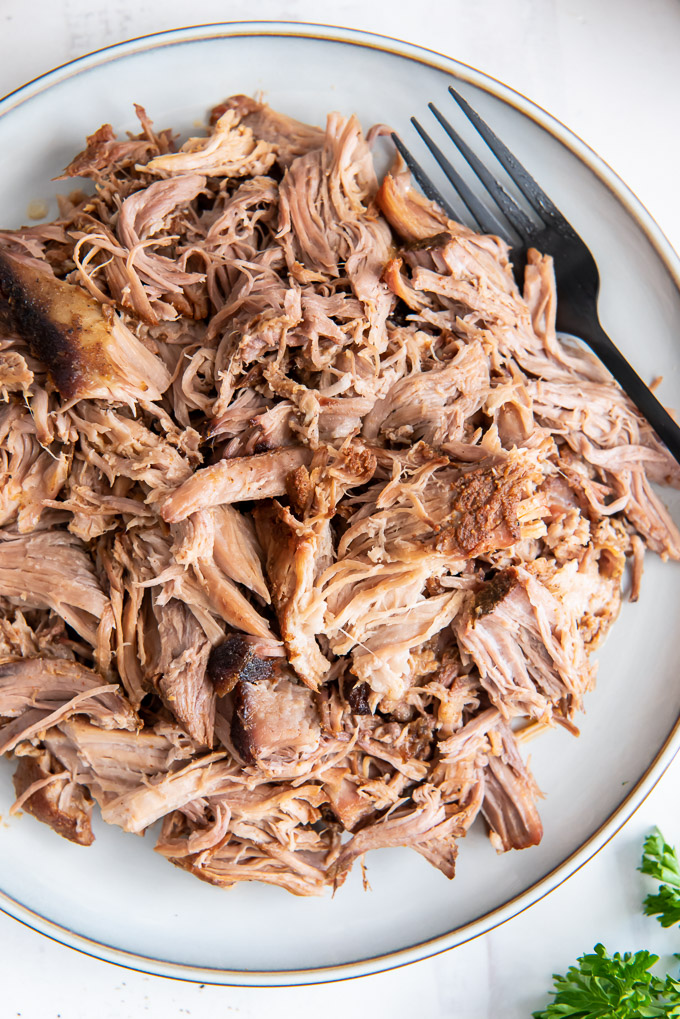 Slow cooker pulled pork on a white plate with a fork