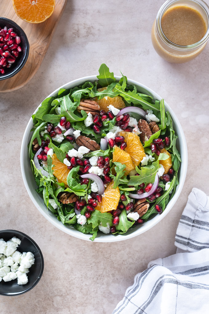 Arugula pomegranate salad in a bowl with pomegranate dressing and linen