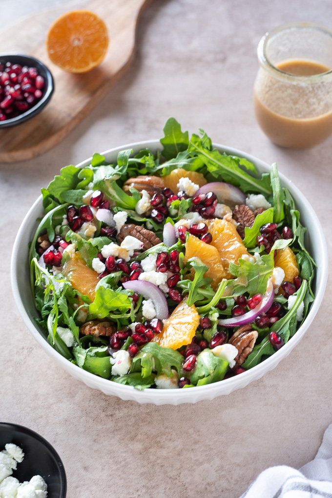 Arugula orange pomegranate salad in a white bowl with pecans on top